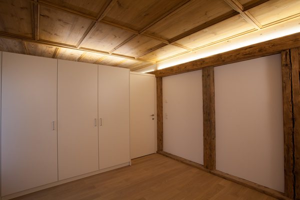 Zimmer unter der ergänzten Täferdecke, Lichtband entlang des alten Unterzugs, rechts freigelegte Holzständer