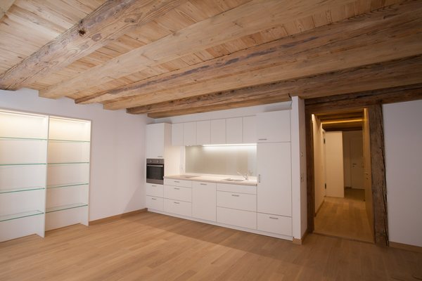 Wohnküche unter der alten Balkendecke, weiße Küchenzeile an der Wand, rechts ein freigelegter Holzständer