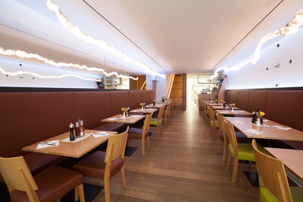 Gastraum des Restaurants im Erdgeschoß, Bankette entlang der Wände, Lichtlinien unter der hellen Decke