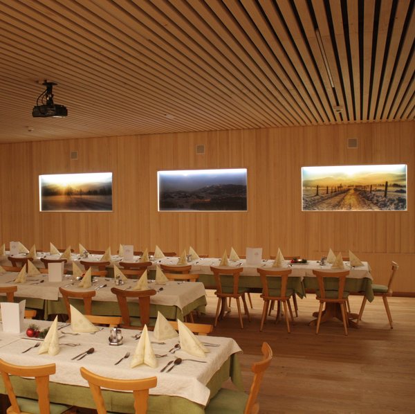 Der Saal, gedeckt, mit Holzverkleidung an Wand und Decke und drei hinterleuchteten Landschaftsbildern