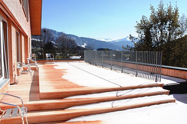Terrasse im Obergeschoß, Holzbelag und Stabgeländer, dahinter die verschneiten Berge