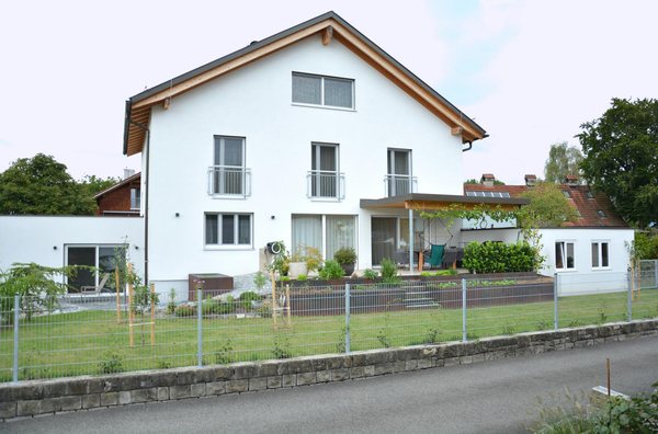 Die Giebelseite mit den hohen Fenstertüren und schmalen Geländern, rechts die überdachte Terrasse