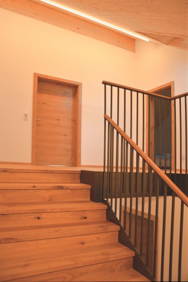 Die Treppe aus Holz mit senkrechtem Stahlgeländer, darüber die sichtbare Holzdecke