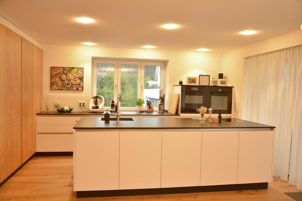 Die zusammengelegte Küche mit Kochinsel und dunkler Arbeitsplatte, Fenster in den Garten