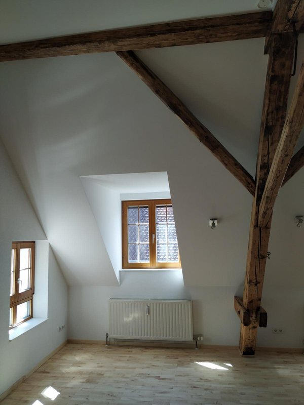 Zimmer unter dem Dach mit dem alten Gebälk und Fenster zur Gasse