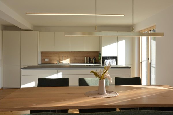 Die Essküche der neuen Wohnung, weiße Zeile mit Holzrückwand und dunkler Arbeitsplatte, Lichtband an der Decke