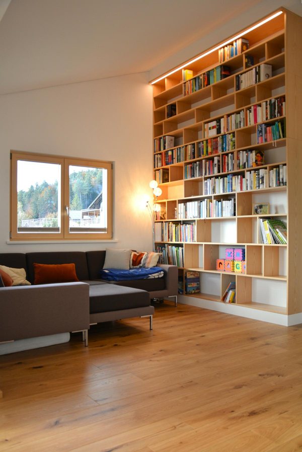 Wohnzimmer mit raumhohem Einbauregal aus Holz, Lichtband über der obersten Reihe