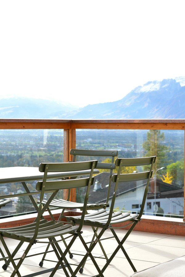 Der Balkon mit Holzhandlauf über der Glasbrüstung, darunter das Tal und die Berge gegenüber