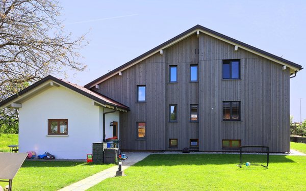 Die Gartenseite mit dem senkrechten Holzschirm über beiden Geschoßen, links der verputzte Anbau