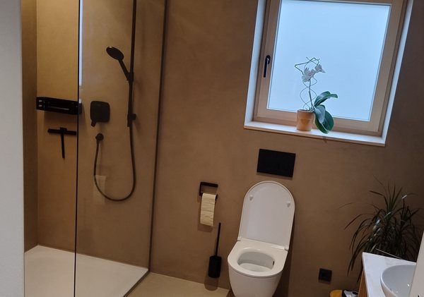 Dusche und WC vor einem fugenlosen braunen Wandbelag, Fenster mit Milchglas