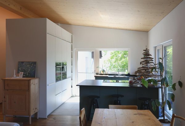 Küche und Essbereich einer Wohnung unter der sichtbaren Holzdecke, rechts die Tür ins Freie